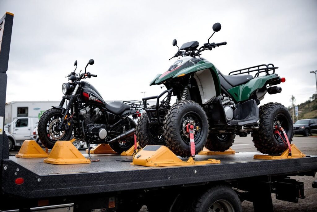 A motorcycle and an ATV securely strapped on a flatbed tow truck, highlighting motorcycle and ATV towing services.